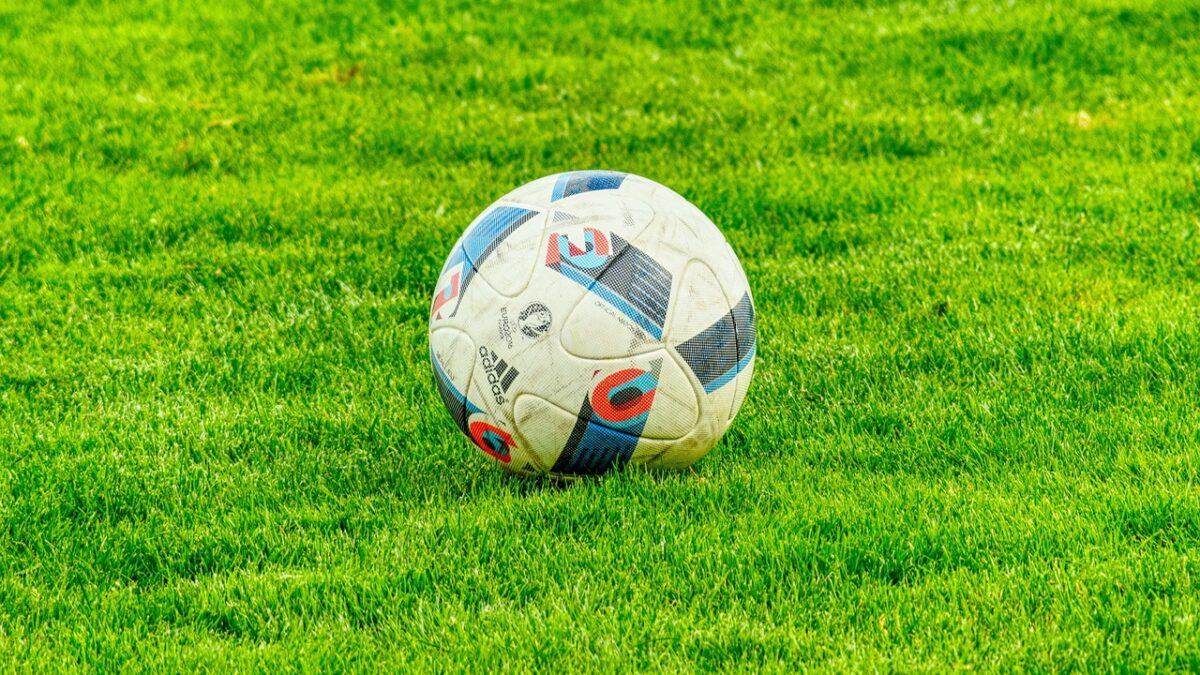 Un ballon de football blanc, bleu et rouge, de marque Adidas, posé sur une pelouse verte.