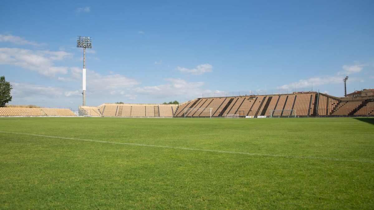 Stade de football vide, pelouse verte et tribunes sous un ciel bleu
