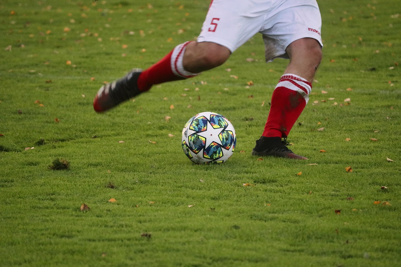 Joueur en chaussettes rouges et blanches frappant un ballon sur une pelouse, vu au niveau des jambes