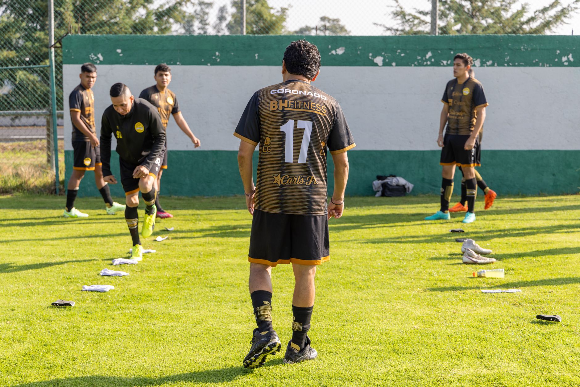 Joueurs de football à l’entraînement sur une pelouse, un joueur vu de dos au maillot numéro 17 au premier plan et d’autres qui s’étirent.