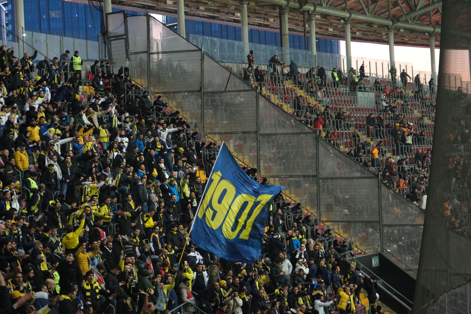 Supporters de football rassemblés dans une tribune de stade, agitant un drapeau bleu et jaune.